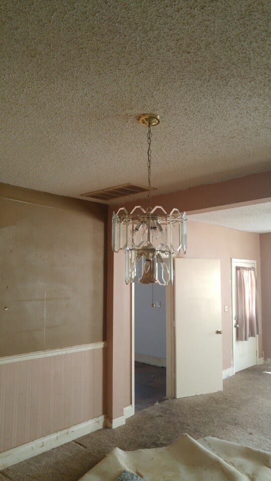 Before: a very outdated chandelier in a room with old wallpaper and carpet